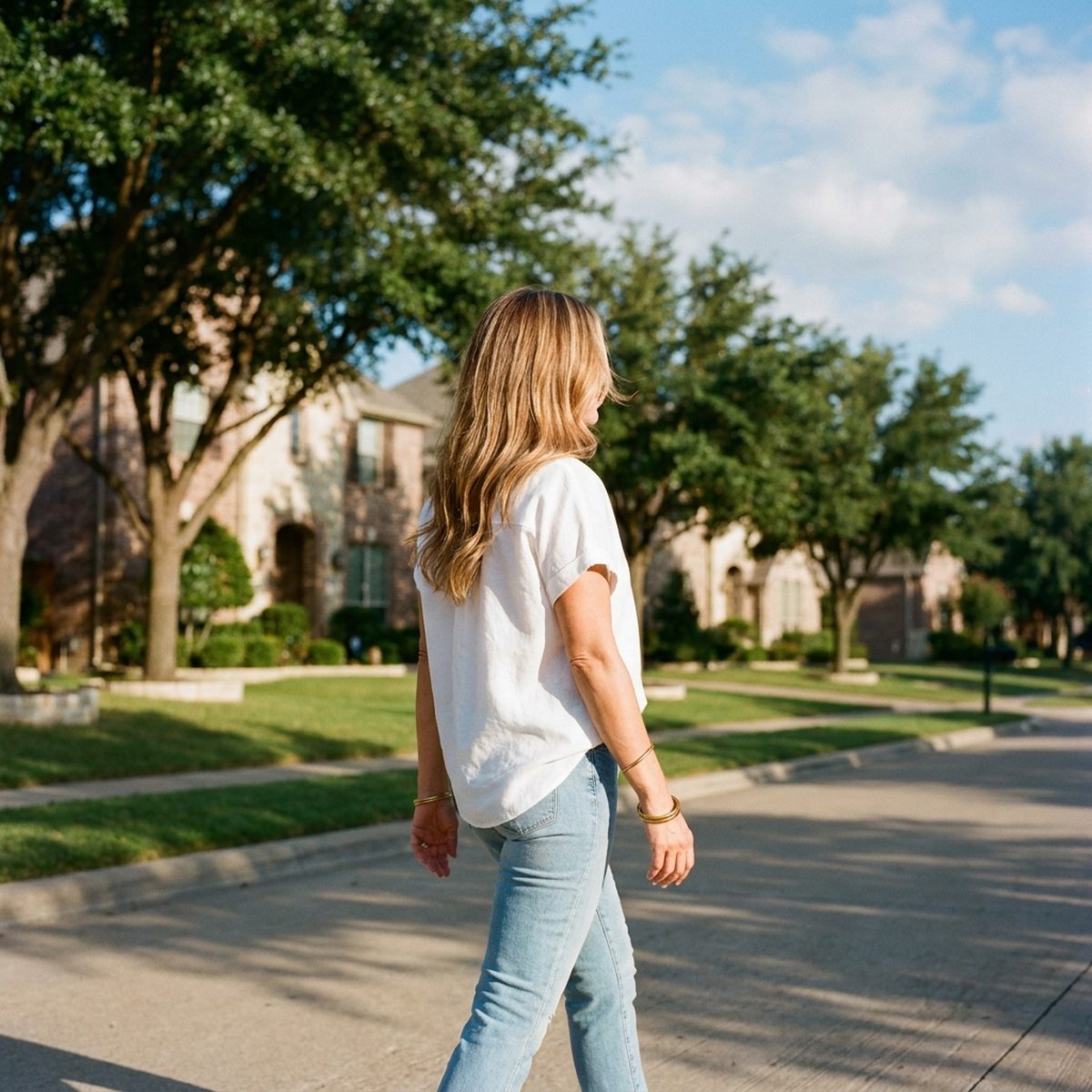 Confident woman in her 40s with dimensional honey balayage walking through a McKinney neighborhood near Stonebridge Ranch, styled by Moxi Hair Studio in McKinney, TX